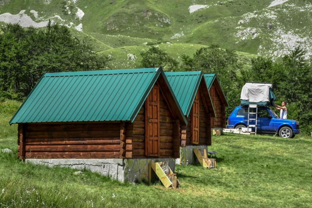 ベラネにあるEko Katun Kolijevkaの緑の屋根と青いトラックが並ぶ丸太小屋