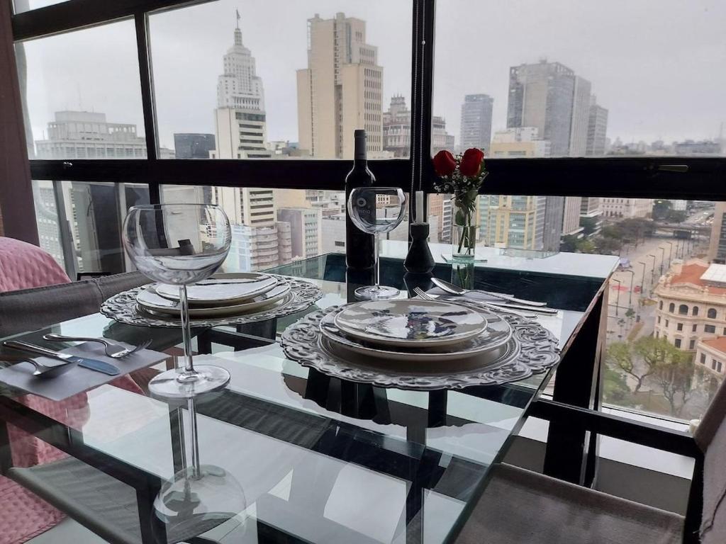 a glass table with plates and wine glasses on a window at Mirante do Serjoca no Centro Histórico in Sao Paulo