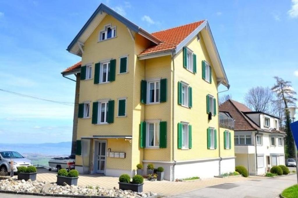 een geel huis met groene luiken erop bij Ferienwohnung Rätia mit Bodenseeblick in Wolfhalden 