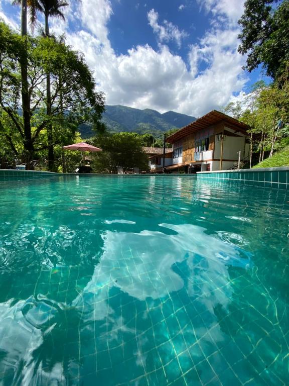 a swimming pool with blue water in front of a house at Pousada Tekoá Indiana in Cachoeiras de Macacu