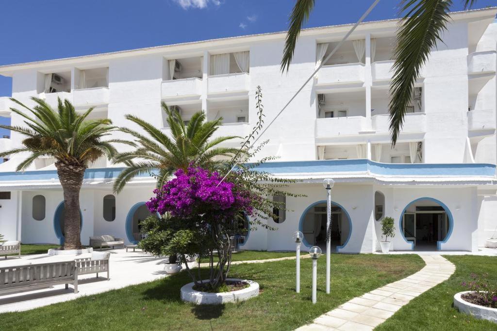 un grande edificio bianco con palme e fiori viola di Sud Hotel Pulsano a Pulsano