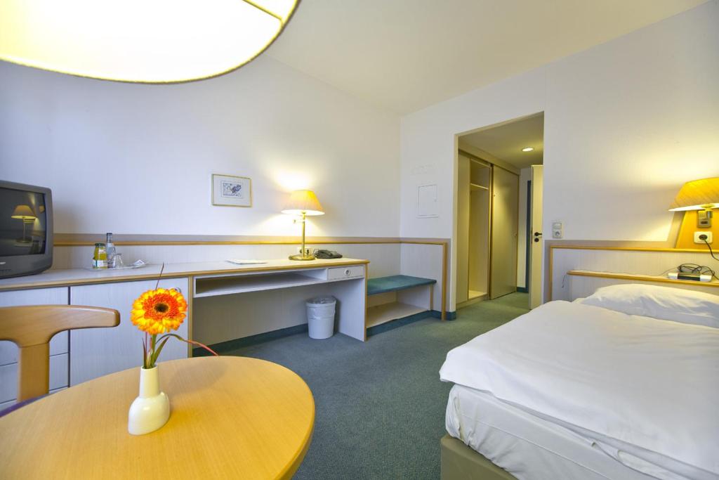 ein Hotelzimmer mit einem Bett und einem Tisch mit einer Blume darauf in der Unterkunft Leine-Hotel in Göttingen