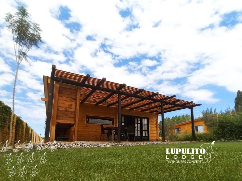 a log cabin with a roof on a grass field at Lupulito Lodge Cabañas de Montaña in Ciudad Lujan de Cuyo