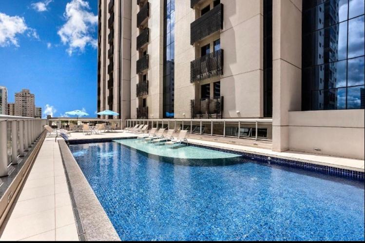 a large swimming pool with white chairs and buildings at FLAT 1417 in Águas Claras