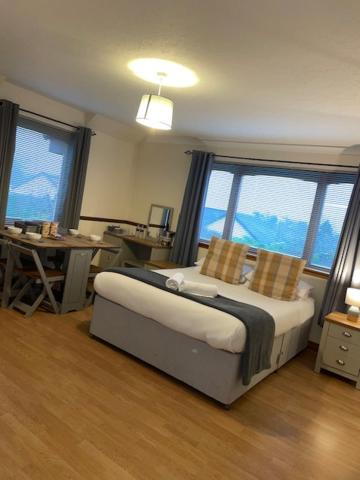 Schlafzimmer mit einem Bett, einem Tisch und Fenstern in der Unterkunft Highland Stays - Rushfield House Rooms in Fort William