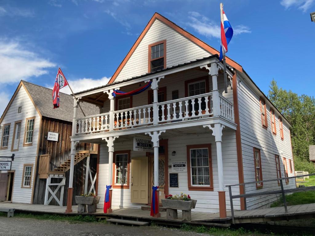 an old white house with two flags on it at St. George Hotel in Barkerville