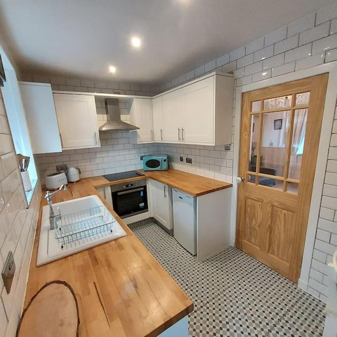 Lovely 1 Bed house in Largs, North Ayrshire في لارغس: مطبخ بدولاب بيضاء وقمة كونتر خشبي