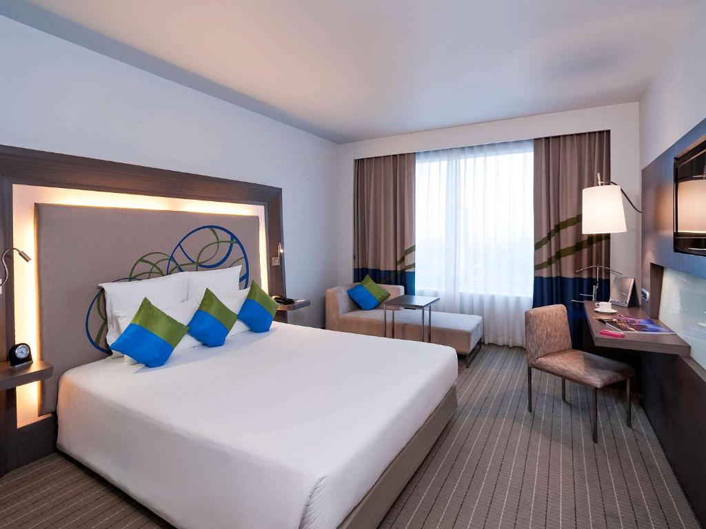 a hotel room with a large white bed and a desk at Novotel Bangkok Ploenchit Sukhumvit in Bangkok
