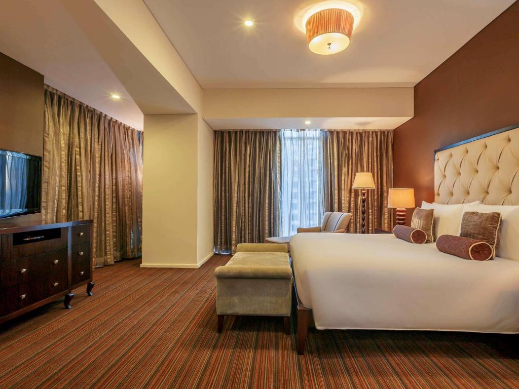 Joy-Nostalg Hotel & Suites Manila Managed by AccorHotels في مانيلا: غرفه فندقيه سرير كبير وتلفزيون