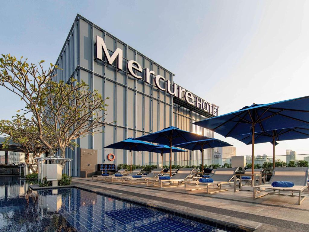 a hotel with chairs and umbrellas next to a swimming pool at Mercure Bangkok Sukhumvit 24 in Bangkok