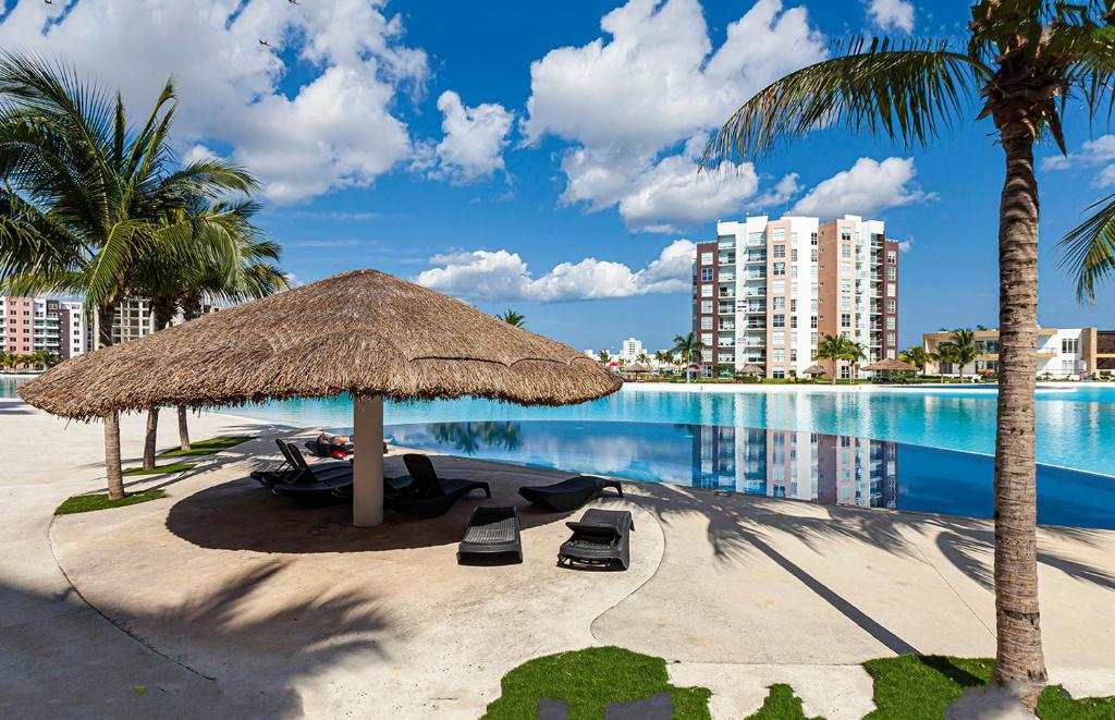 a beach with a straw umbrella and chairs and a swimming pool at Departamento 'Hozanek' en Dream Lagoons Cancun in Cancún