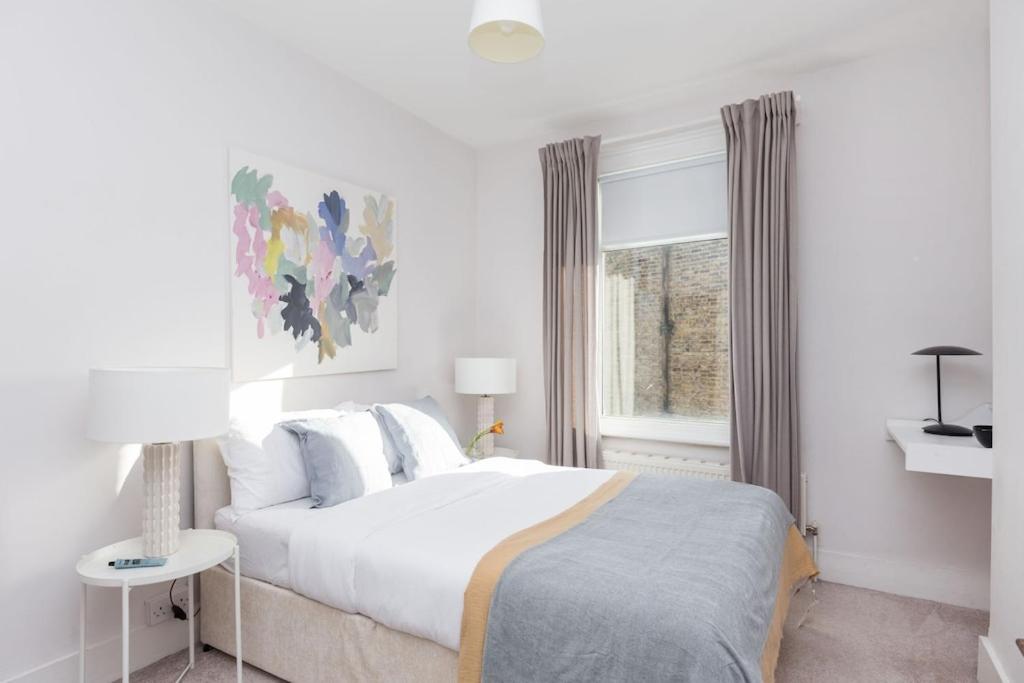a white bedroom with a bed and a window at Newly renovated large 4/5 bedroom Victorian terrace house with garden. in London