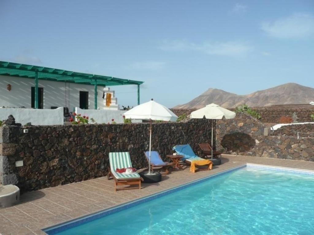 a pool with chairs and umbrellas next to a wall at Finca mit Pool und herrlichem Meerblick in Playa Blanca