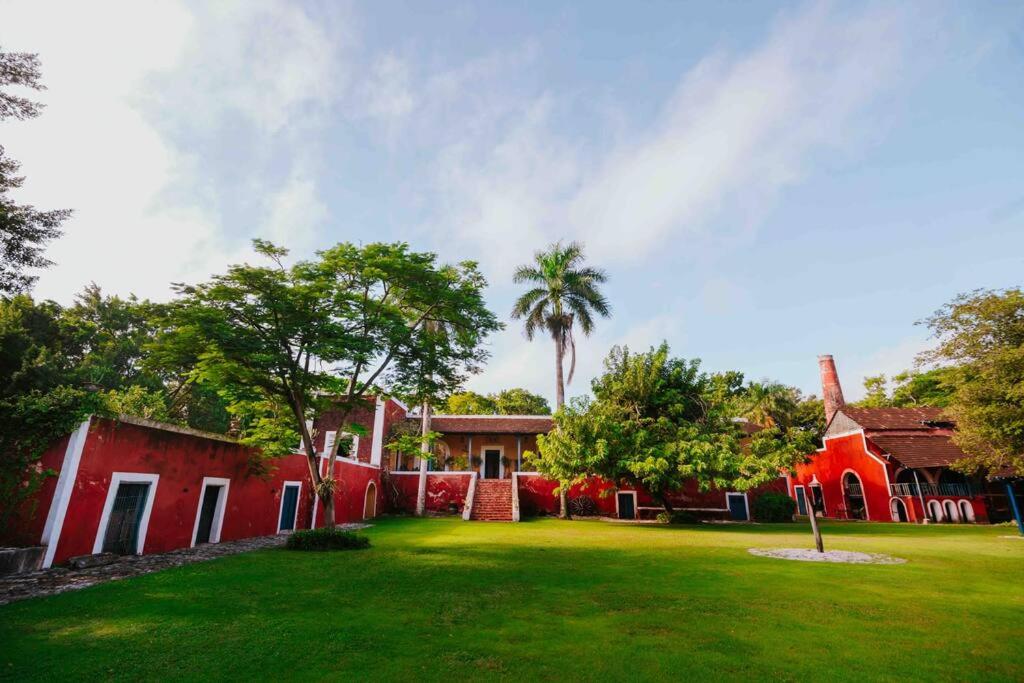 a red house with a green yard and a palm tree at Hacienda extraordinaria, jardines preciosos y pirámides 