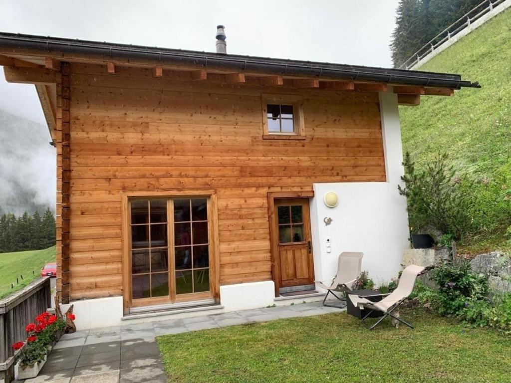 una casa de madera con 2 sillas delante en Neuwertiges 2-Zi-Ferienchalet 55m2, en Monstein