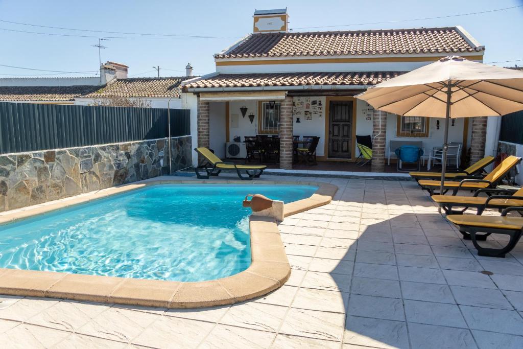 a swimming pool with an umbrella and chairs and a house at Casa da Ti´Lola in Évora