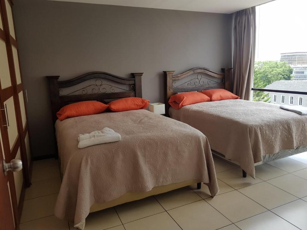 1 dormitorio con 2 camas con almohadas de color naranja y ventana en Apartamento Reforma Ciudad de Guatemala, en Guatemala
