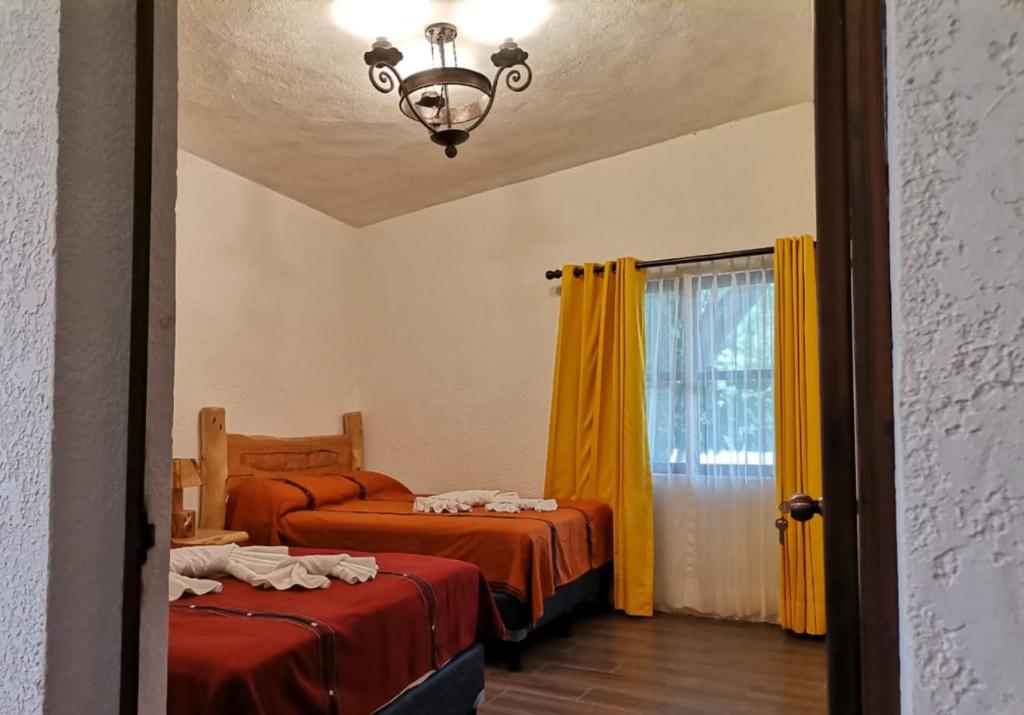 a bedroom with two beds and a window with yellow curtains at Hotel del Bosque in Panajachel