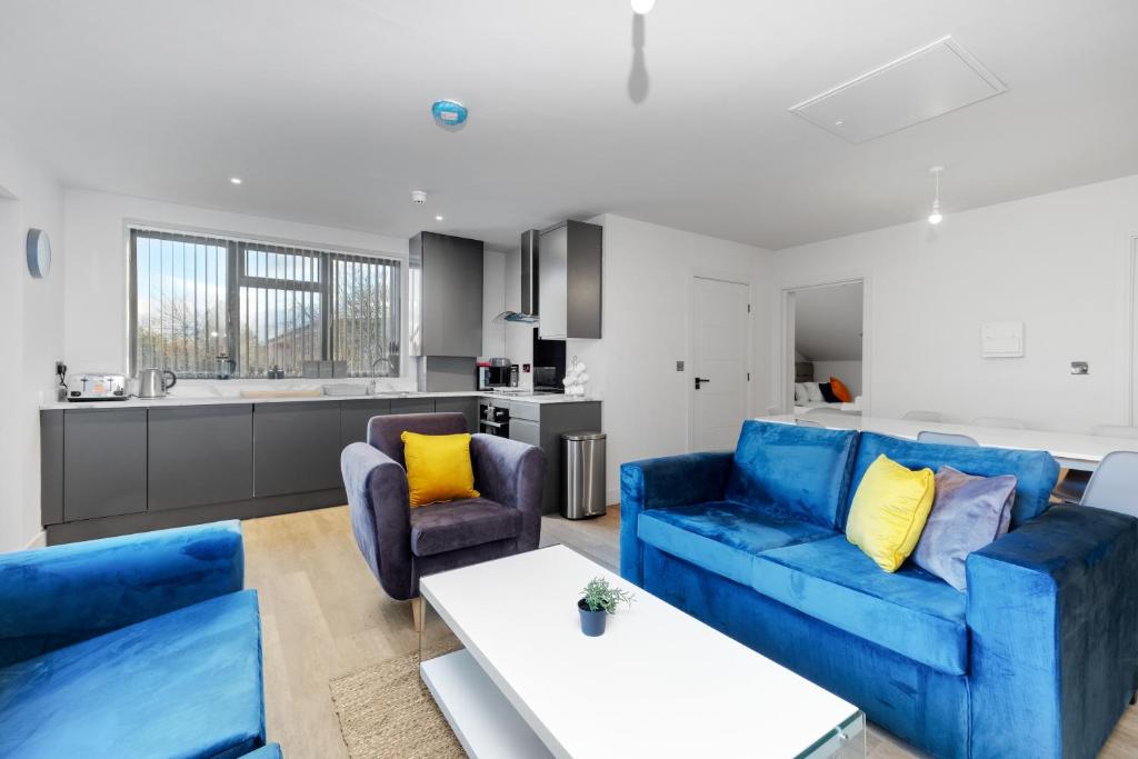 a living room with blue couches and a kitchen at Infra Mews, Superb Delightful Apartments Perfect for Contractors & Long Stays, 1, 2 & 4 Bedroom, WiFi & Parking in Milton Keynes
