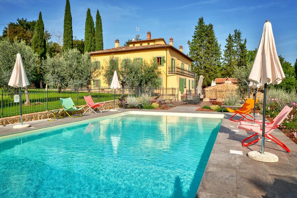 a pool with chairs and umbrellas in front of a house at Villa Maria in Monte San Savino