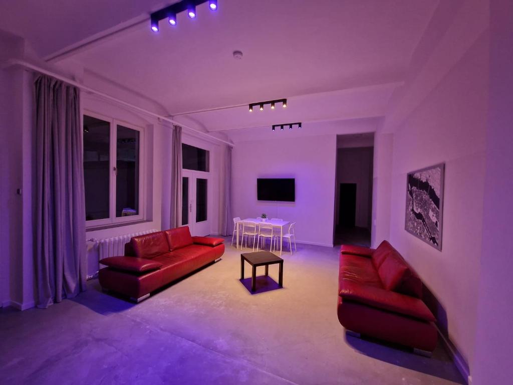 RAJ Living - 300m2 Loft with 7 Rooms - 15 Min Messe DUS & Old Town DUS في دوسلدورف: غرفة معيشة بها كنبتين حمراء وطاولة