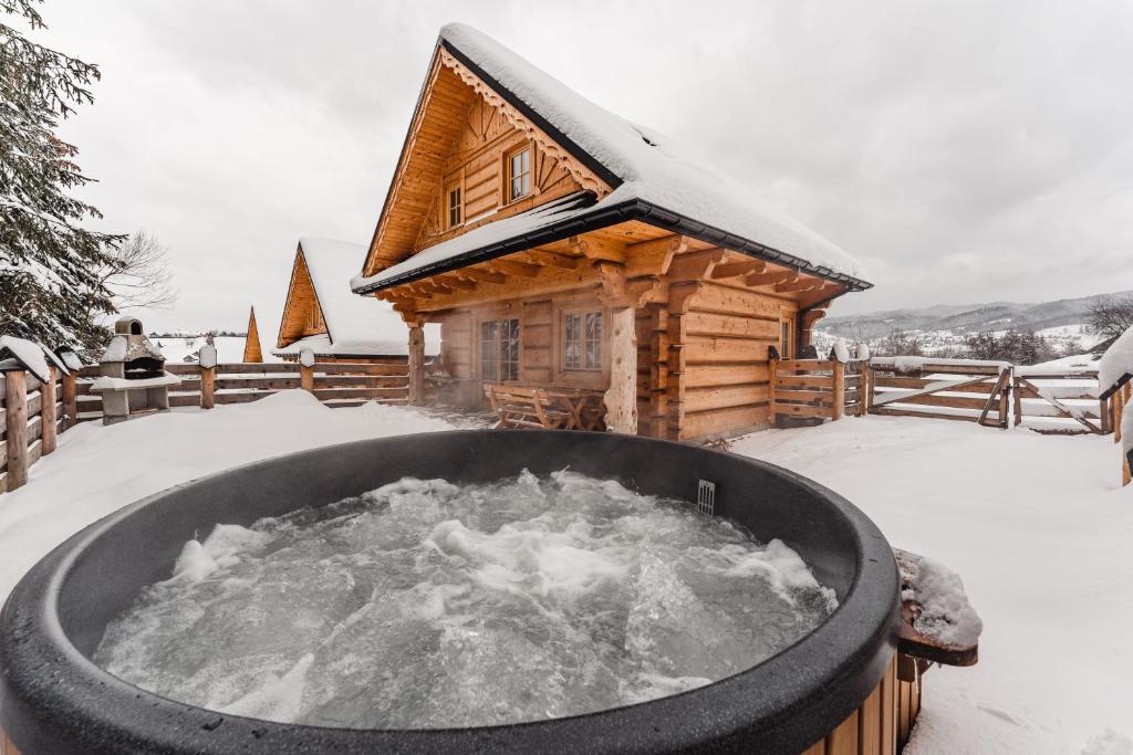 a hot tub in front of a log cabin in the snow at Pienińska Przystań in Kluszkowce