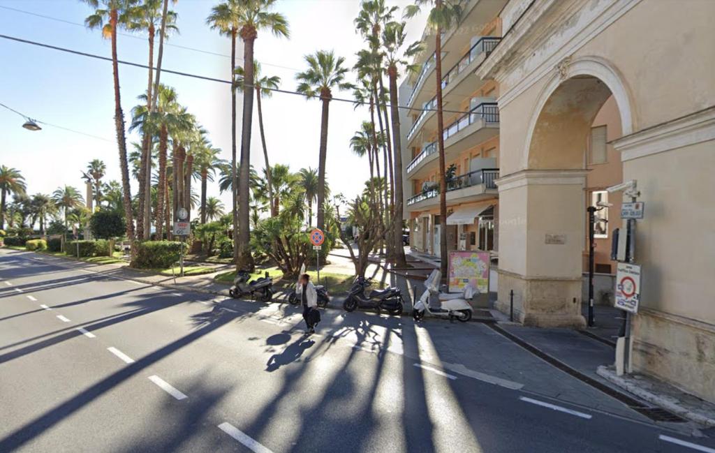 eine Person, die eine Straße mit Palmen und einem Gebäude entlang geht in der Unterkunft Appartamento Elisa 100 metri dal mare in Finale Ligure