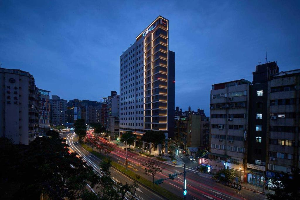 un edificio alto en una calle de la ciudad por la noche en Boutech JianTan Hotel, en Taipéi