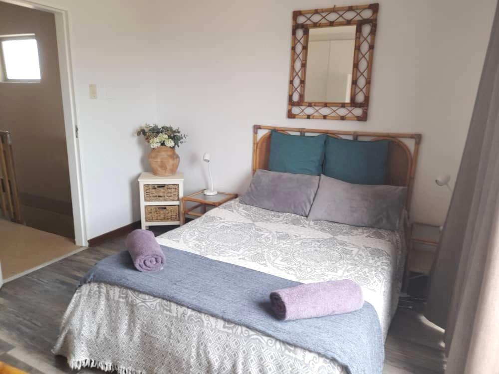 Schlafzimmer mit einem Bett mit lila Kissen und einem Spiegel in der Unterkunft Beachfront Selfcatering in Henties Bay