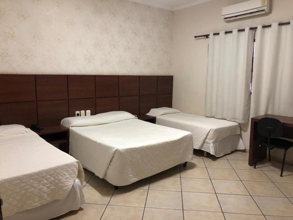 Cette chambre comprend 3 lits, une table et un bureau. dans l'établissement Hotel Residence, à Dourados