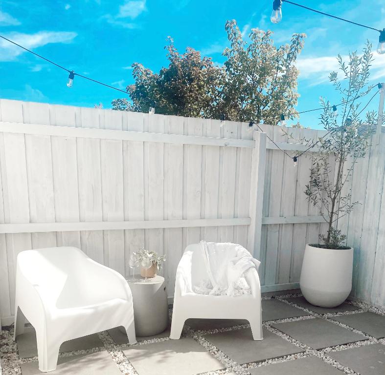 un patio con 2 sillas blancas y una valla en The Hideaway - Guest House, en Warrnambool