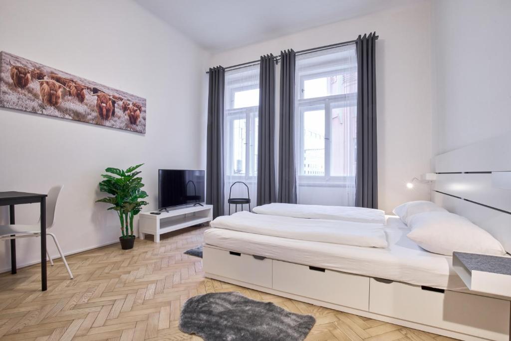 a white bedroom with a large bed and a tv at Archibald Flats Prague in Prague