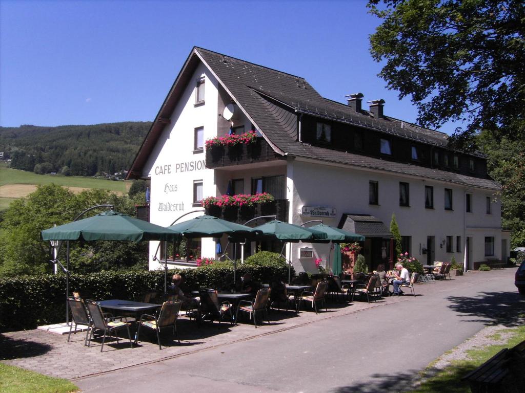 un edificio bianco con sedie, tavoli e ombrelloni di Cafe-Pension Waldesruh a Willingen