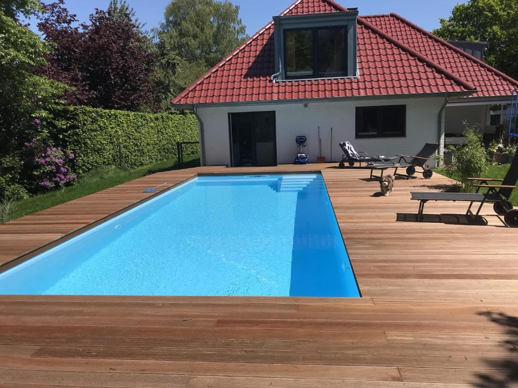 a swimming pool with a wooden deck and a house at Haus Kuestenperle in Schiffdorf