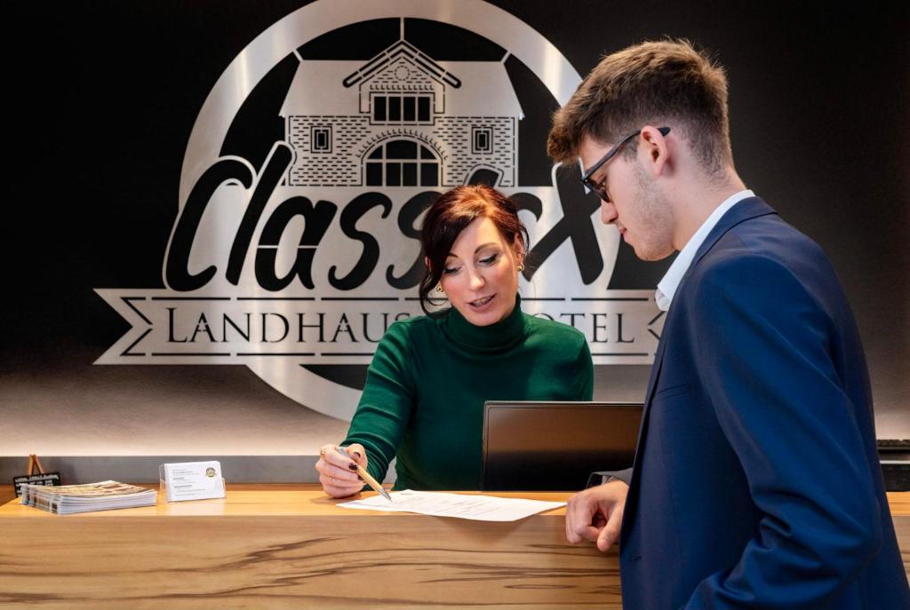 un hombre y una mujer sentados en una mesa firmando en ClassicX Landhaus & Hotel - Bed & Breakfast, en Gensingen