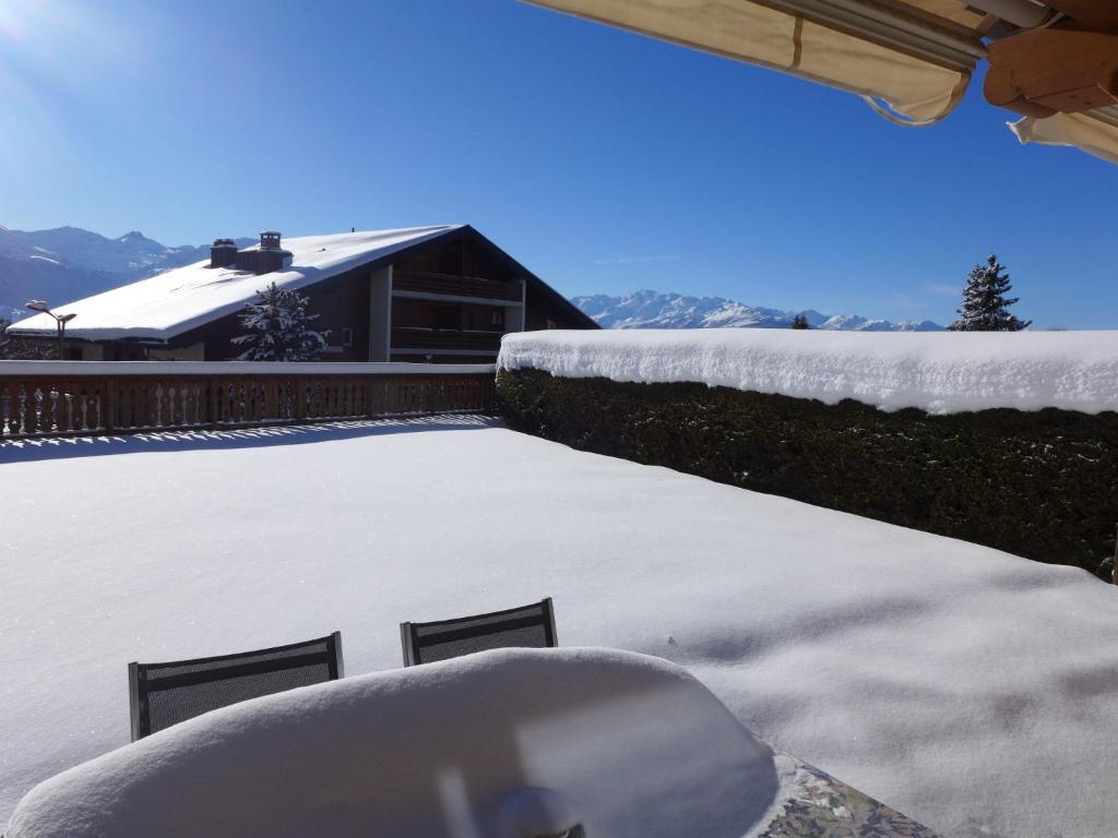 a snow covered patio with a house in the background at Apartment Antares R05 by Interhome in Crans-Montana