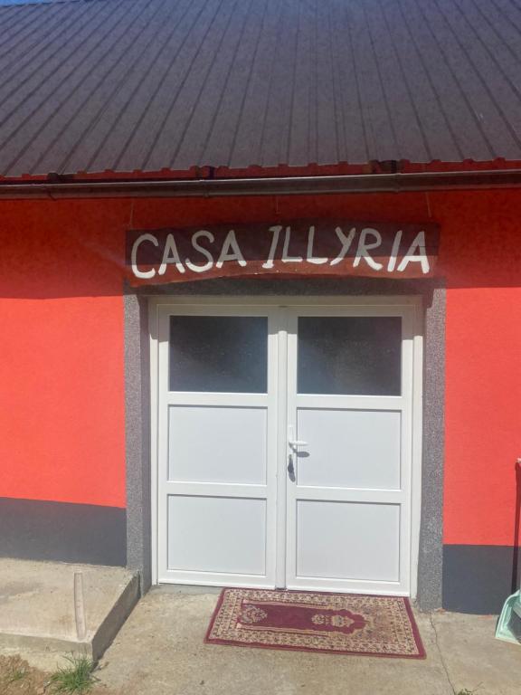 un bâtiment avec une porte de garage blanche et un panneau au-dessus. dans l'établissement Casa Illyria, à Gusinje