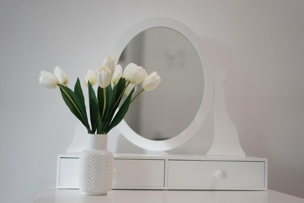 een witte vaas met witte bloemen voor een spiegel bij Apartman ERIK in Požega