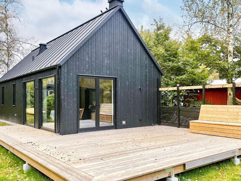 ein schwarzes Haus mit einer Holzterrasse im Hof in der Unterkunft Holiday home HJÄRNARP III in Hjärnarp