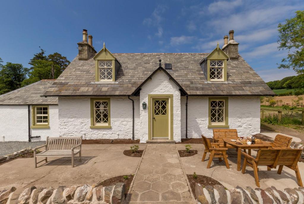 una cabaña con mesa y sillas frente a ella en Home Farm Cottage, en Stranraer