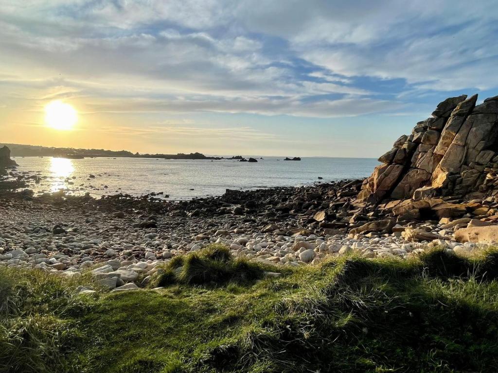 a rocky beach with the sun setting over the water at Premium holiday home in top location with sea view, Plougasnou in Plougasnou