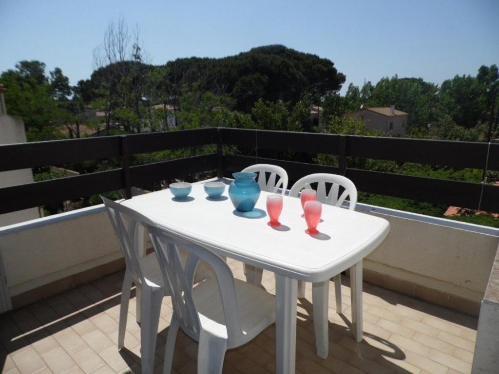 une table et des chaises blanches avec des verres sur le balcon dans l'établissement Studio cab. climatisé avec terrasse, pk privé et piscine - Grau d'Agde - FR-1-423-35, au Grau-dʼAgde