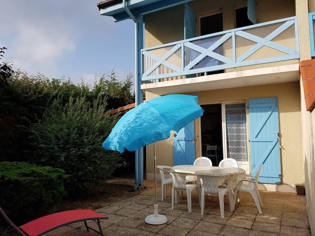 une table avec un parapluie bleu devant une maison dans l'établissement Charmante villa patio avec terrasse - 2 chambres - au port de Capbreton - FR-1-413-126, à Capbreton