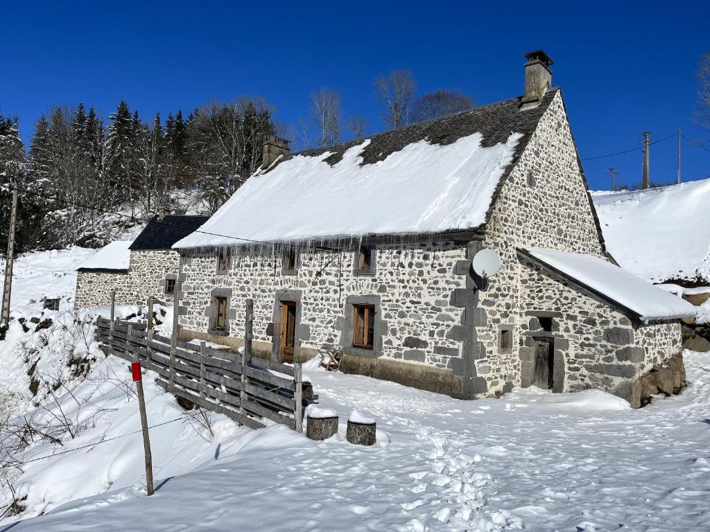 un edificio de piedra con nieve en el techo en Propriete de 6 chambres avec jardin amenage et wifi a Chastreix a 8 km des pistes, en Chastreix