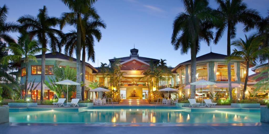 a resort with a pool and palm trees at night at Couples Negril in Negril