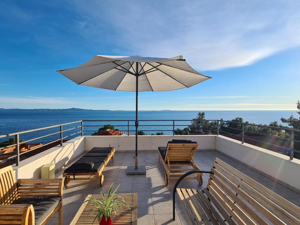 a patio with benches and an umbrella overlooking the ocean at Apartments Toro in Sveta Nedelja