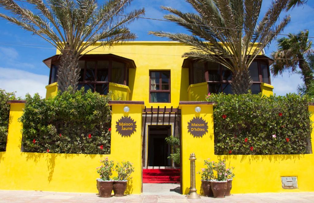 une maison jaune avec deux palmiers devant elle dans l'établissement La Maison Jaune Dakhla Maison d'hôtes, à Dakhla