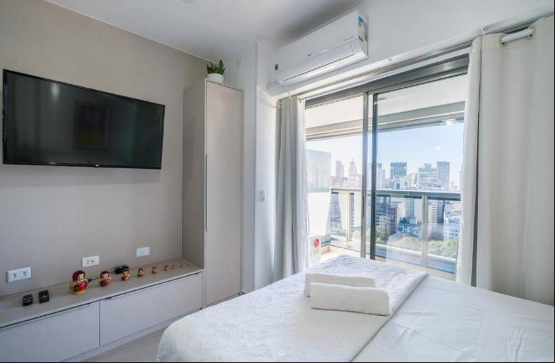een witte slaapkamer met een groot raam en een flatscreen-tv bij Studio vista para cidade in Sao Paulo