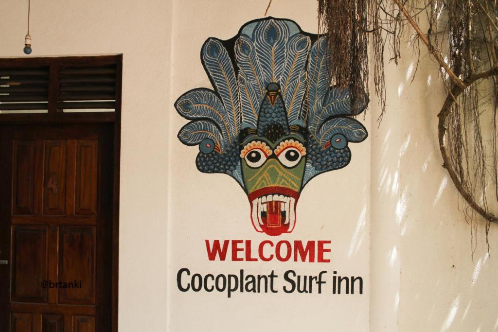 a sign on the side of a building with a head at Cocoplant Surf Inn in Midigama
