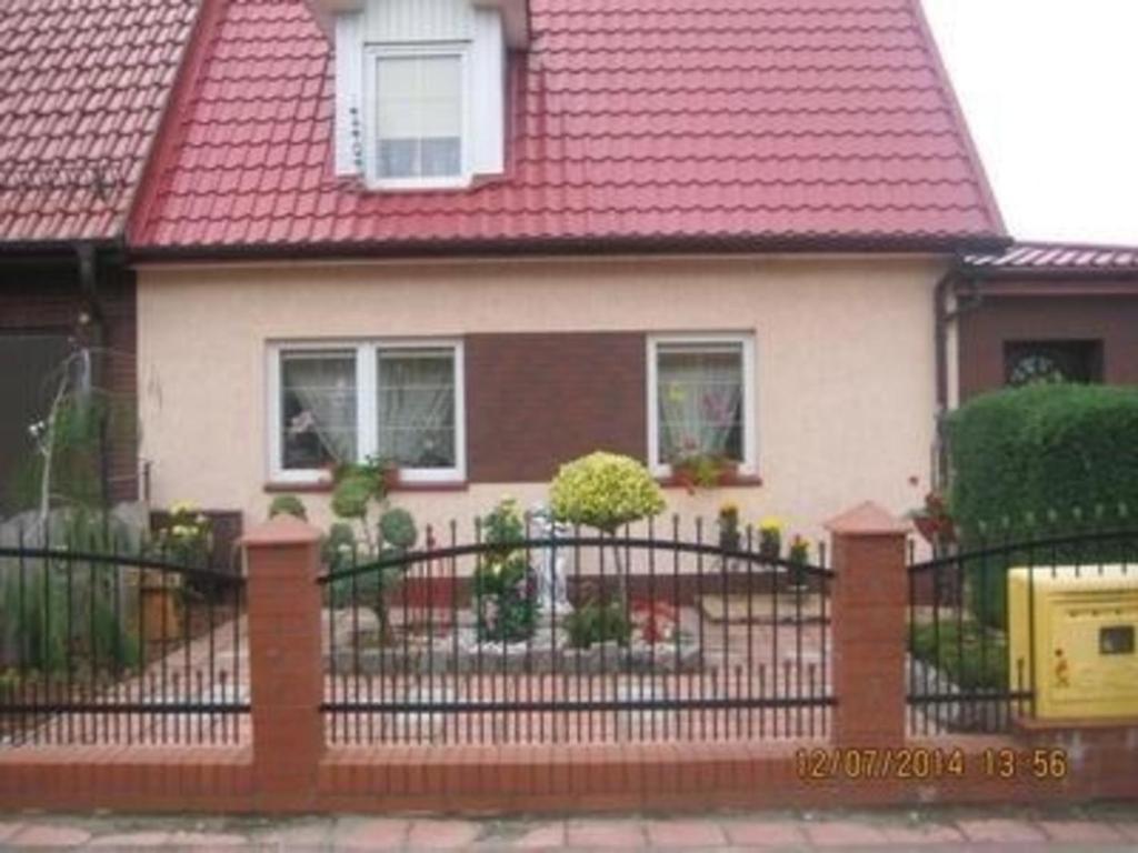 a house with a red roof and a black fence at Ferienhaus in Kolberg mit Grill, Terrasse und Garten in Kołobrzeg